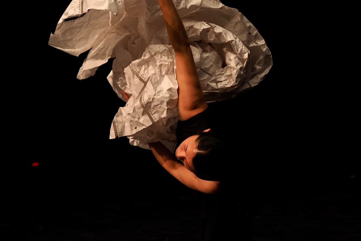 A dancer in a white costume suspended upside down on stage