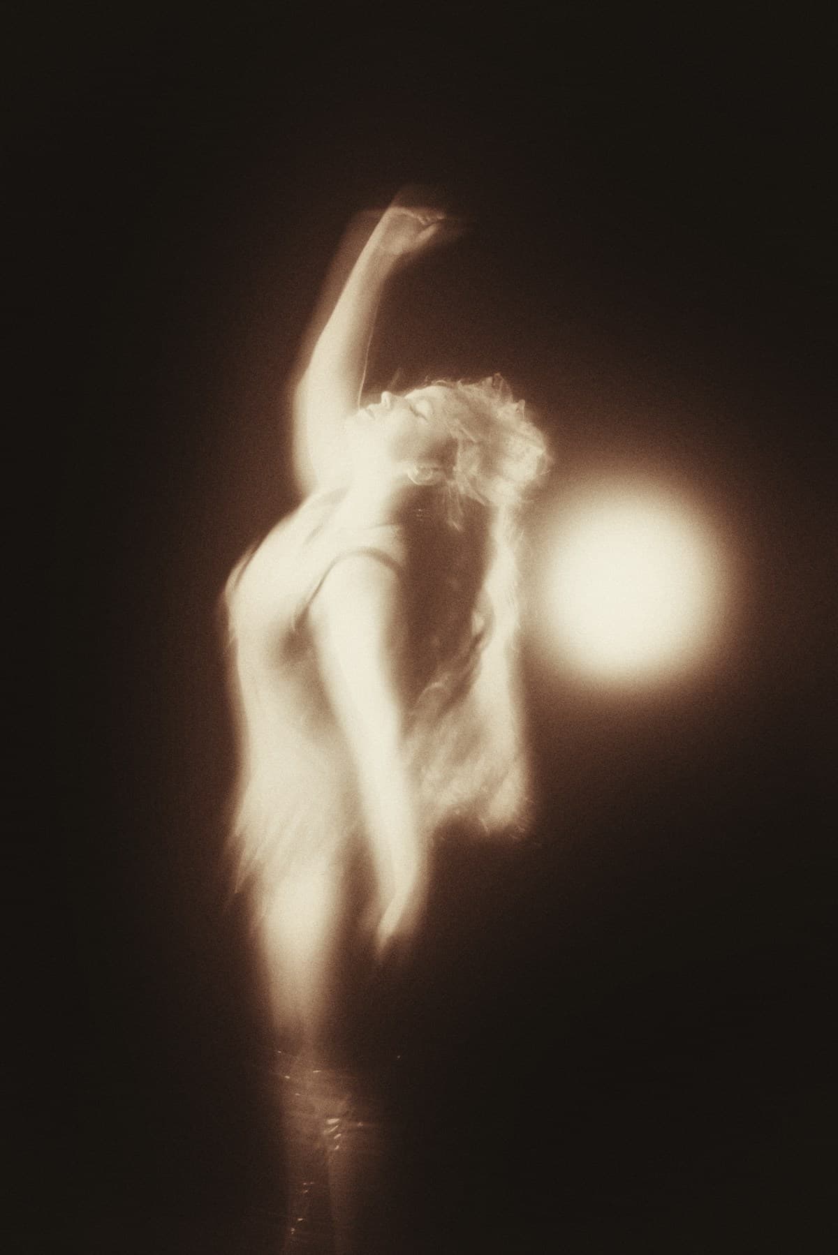 A dancer in motion blur with arms raised against a dark background